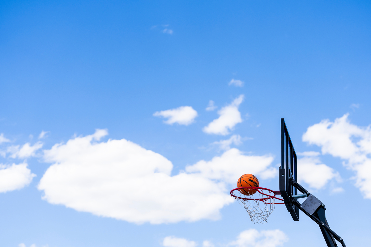 Basketball dropping into basketball net set against a blue sky